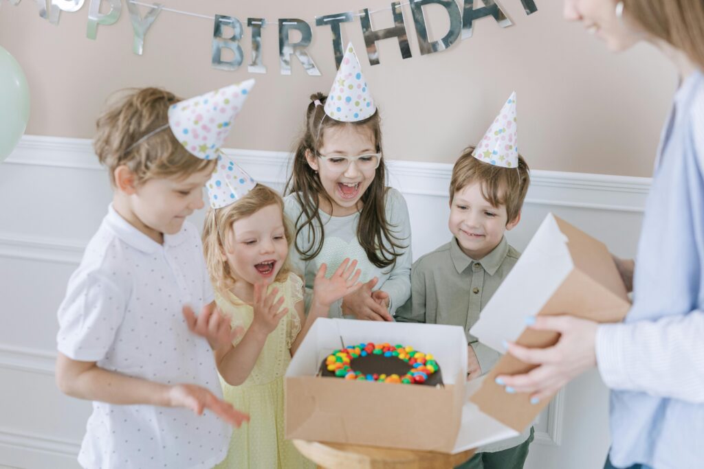 Joyful kids celebrating a birthday with a colorful cake and party hats indoors.